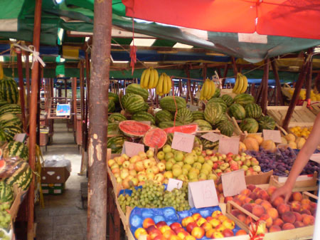 Marktstand mit Obst und Gemüse unter einer roten Plane.