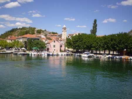 Der Ort Skradin am Wasser, Boote am Kai, dahinter ein Kirchturm.